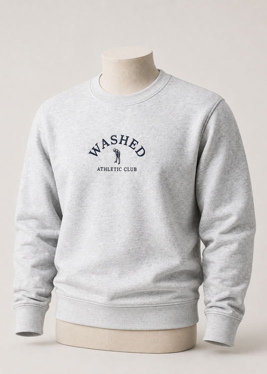 A light heather gray crewneck sweatshirt displayed on a beige mannequin torso against a neutral light gray background. The front of the sweatshirt features a dark navy blue graphic that reads 'WASHED ATHLETIC CLUB' with a small golfer silhouette.